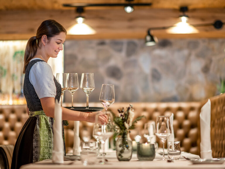 Bedienung in Dirndl stellt Weinglas auf Tisch im Restaurant im Wellnesshotel Hüttenhof Bedienung in Dirndl stellt eines der Weingläser von Ihrem Tablet auf Tisch in modernem Restaurant