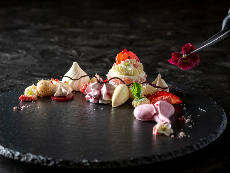Kunstvolles Dessert auf runden Platte wird mit Pinzette mit Blumen verziert